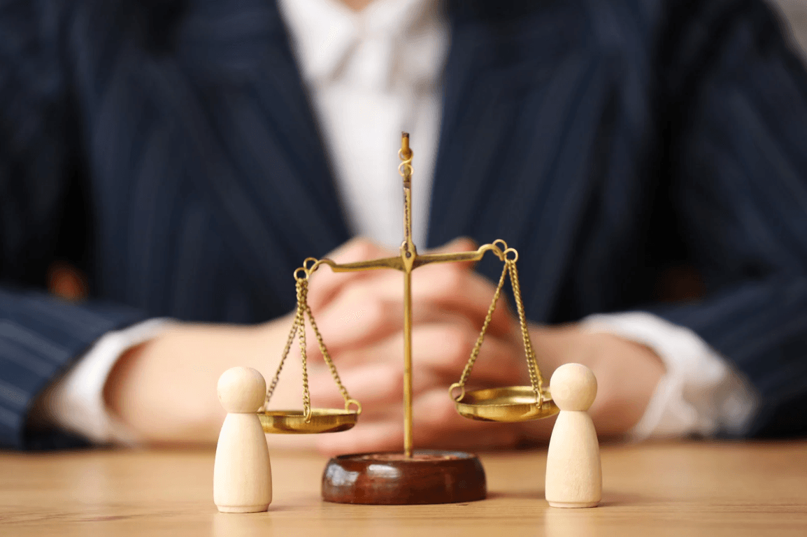 Goldene Waage der Gerechtigkeit und zwei Holzfiguren vor einer Person in einem dunklen Anzug.